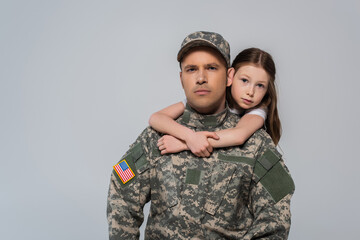 preteen girl hugging brave father in army uniform during memorial day isolated on grey.