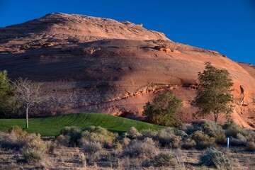 Rocky red hill with trees under a blue sky with clouds.