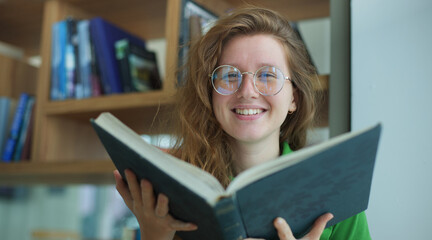 Happy girl, young woman read book in library, college or university student prepare to exam in glasses and smile