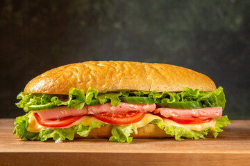 Tasty homemade sandwich on wooden cutting board on black distressed background