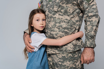 preteen girl hugging brave father in uniform during memorial day isolated on grey.