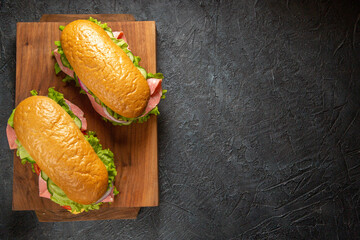 Top view of homemade sandwiches on wooden cutting boards on black distressed background