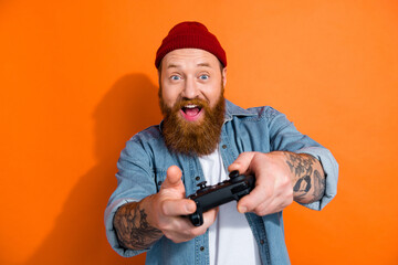 Photo of funny young man red hair beard hold wireless joystick crazy cyber player video game have fun free time isolated on orange color background