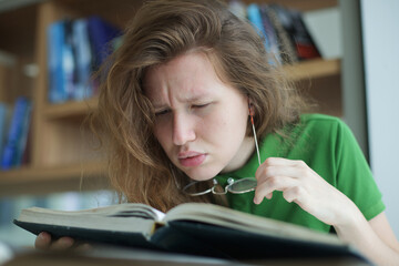 tired overworked, exhausted young woman in glasses college or university student is study hard in library, lesson, problem with eyes, myopic purblind. Vision eyes problems, myopia, blindness.  - obrazy, fototapety, plakaty