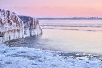 Idyllic frozen huge rock in the middle of the sea with pink sky on the horizon