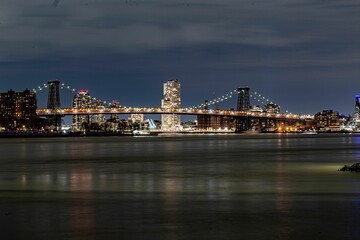 Naklejka na ściany i meble Brooklyn Bridge illuminated with lights at night on the background of the modern cityscape