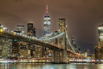 Brooklyn Bridge illuminated with lights at night on the background of the modern cityscape