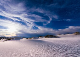 Swirling clouds in a blue sky over white sand dunes