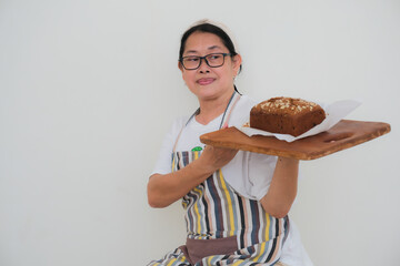 Asian baker lifting up a hot loaf of freshly baked fruit cake from the oven, using wooden tray