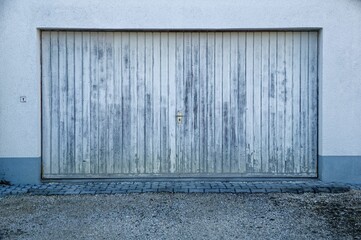 Aged metallic garage door that is beginning to peel and a gravel driveway with a weathered stone