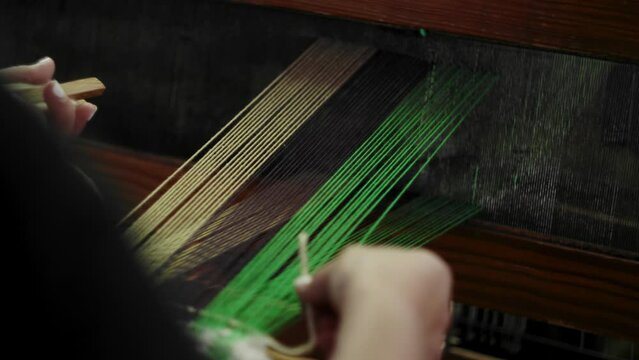 Woman adjusts shuttle after weaving through loom, pulls to close loom