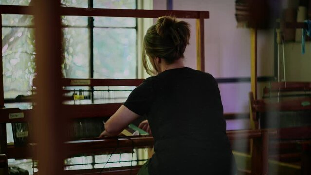 Cinematic view of woman working hand weaving loom, upper body rear view