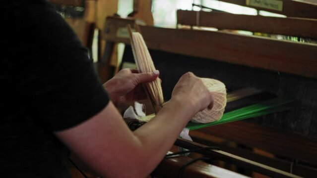 Woman prepares shuttle for loom by wrapping neutral brown colored yarn from spool
