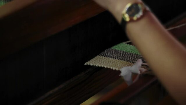 Woman moves shuttle through green and black yarn, working on loom, medium angle