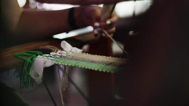 Skilled loom weaver works with hands moving shuttle and loom with green black yarn
