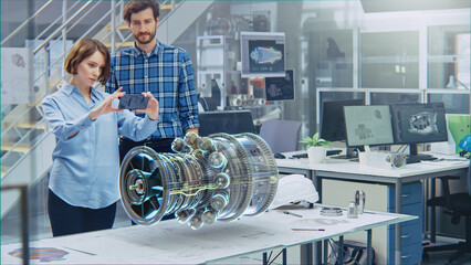 Industry 4.0 Facility: Female Designer with Chief Engineer Use Smartphone with Augmented Reality App to Manipulate 3D Engine. Specialists Working on Eco-Friendly Green Energy Turbine Concept.