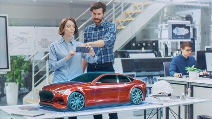Industrial Design: Automotive Engineer and Designer Working on 3D Electric Car Prototype, Using Smartphone with Augmented Reality. Graphical Engine, Battery, Chassis, Body Collect into Vehicle