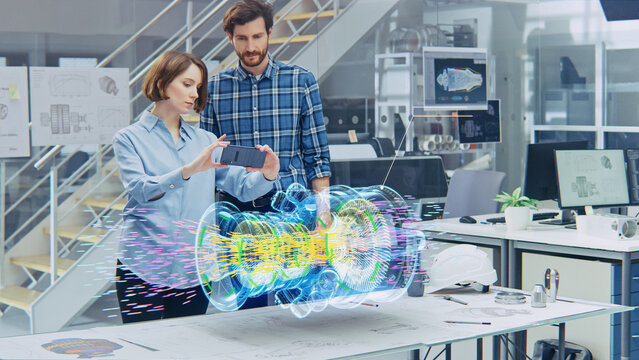 Engineering Facility: Female Designer with Lead Engineer Use Smartphone with Augmented Reality App to Manipulate 3D Engine. Specialists Working on Eco-Friendly Green Energy Turbine Concept