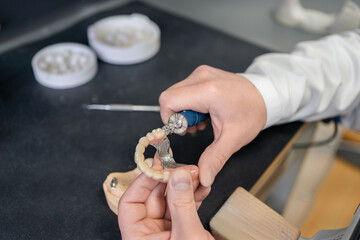 Unrecognizable male technician working in lab and using polishing machine for producing denture