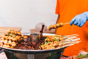 Food vendor hand holding pork meatballs in skewer with sweet chili sauce.
