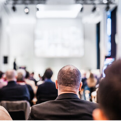 Fototapeta premium Speaker giving a talk in conference hall at business event. Rear view of unrecognizable people in audience at the conference hall. Business and entrepreneurship concept