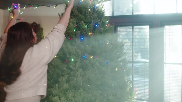 Beautiful girl decorating a huge Christmas tree with garlands in the living room for the new year