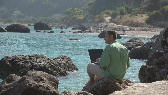 Man with laptop on the beach rocks, "workation" work in vacation concept