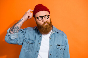 Photo of uncertain funky guy dressed denim jacket eyeglasses finger head looking empty space isolated orange color background