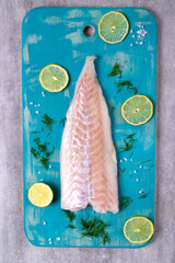 Raw cod fillet on turquoise colored wooden board with lime slices and salt. Fresh seafood...