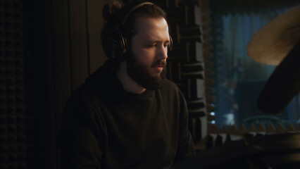 Obraz premium Male musician in headphones plays a drum kit. Drummer records song for musical rock band album in sound recording studio. Work in the music recording room. Music production concept. Zoom in.