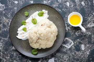 Plate with steamed cauliflower head and cream-cheese, top view on a dark-brown granite background, horizontal shot