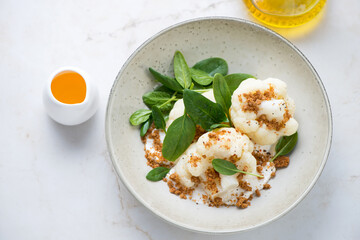 Beige plate with steamed cauliflower florets, ricotta and fresh spinach, high angle view on a light-beige marble background, horizontal shot