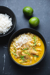 Black bowls with fish yellow curry and white rice, vertical shot on a black marble background, elevated view, selective focus