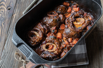 Braised beef shanks or ossubuco in roasting pot on wooden table. 