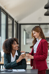 Young Asian and African businesswoman African woman relaxing with coffee mug while brainstorming investment plan Financial business together in the office management concept.