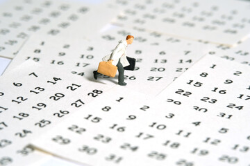 Miniature tiny people toy figure photography. A businessman running above calendar schedule...