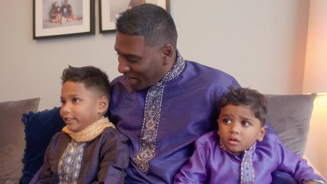 MS Father and sons (2-3, 6-7) sitting on sofa in traditional clothing