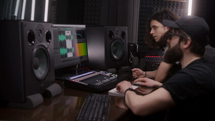 Sound engineer and musician create song in music recording room. Computer screen showing DAW...