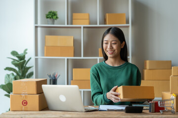 Fototapeta na wymiar Asian female startup business owner She smiled and was delighted to receive an online order from a customer showing her information on her laptop to prepare parcels for delivery through the company.