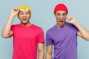 Young surprised shocked overjoyed fun stylish cheerful fun couple two friends men wear casual clothes together lower glasses looking camera isolated on pastel plain light blue cyan background studio.