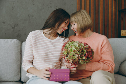 Two lovely adult women mature mom young kid in casual clothes present box with gift ribbon bow sit on gray sofa couch stay at home flat rest relax spend free spare time in living room Family concept - Powered by Adobe