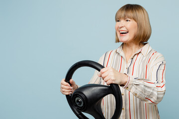 Side view elderly satisfied happy woman 50s years old wear striped shirt hold steering wheel driving car isolated on plain pastel light blue cyan color background studio portrait. Lifestyle concept.