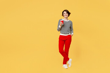 Fototapeta na wymiar Full body smiling young woman wear casual black and white shirt hold takeaway delivery craft paper brown cup coffee to go isolated on plain yellow color background studio portrait. Lifestyle concept.