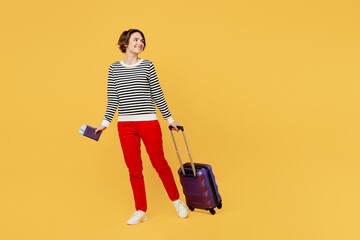 Traveler woman wears casual clothes hold suitcase passport ticket look aside isolated on plain yellow background studio. Tourist travel abroad in free spare time rest getaway Air flight trip concept.