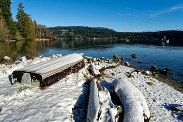 Scenic winter scene featuring an upside down boat on a beach and a tranquil lake