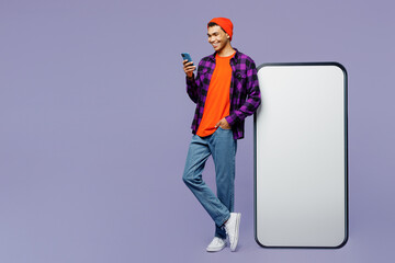 Full body young man wear casual shirt orange hat big huge blank screen mobile cell phone with workspace copy space area using smartphone browsing internet isolated on plain pastel color background.