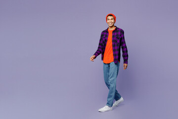 Fototapeta premium Full body smiling happy cheerful young man of African American ethnicity wear casual shirt orange hat walking going look camera isolated on plain pastel light purple color background studio portrait.