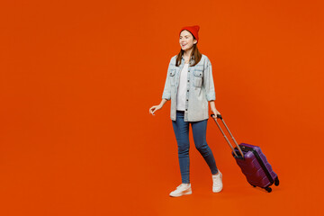 Traveler woman wearing casual clothes hold suitcase walking going isolated on plain red orange color background. Tourist travel abroad in free spare time rest getaway Air flight trip journey concept.