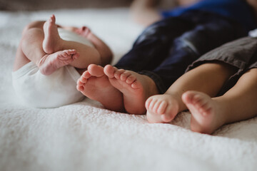 three children's feet on on a bed with a newborn baby