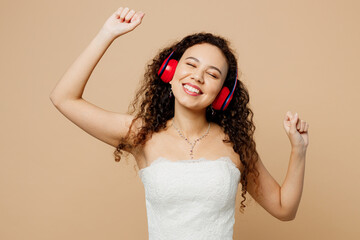 Happy smiling young woman bride wear wedding dress posing headphones listen to music raise up hands...
